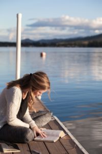 a young woman reading at the lake
